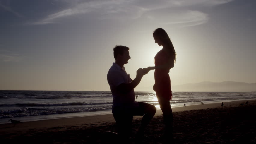 Silhouette Of Man Proposing To Woman On Beach On His Knee Couple Silhouette Of Man Proposing To Woman On Beach On His Knee Couple
