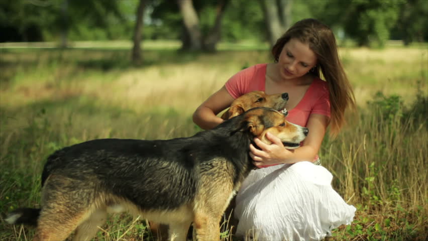 A Pretty Girl In A Wooded Field Kneeling Down Petting Two Dogs On A ...